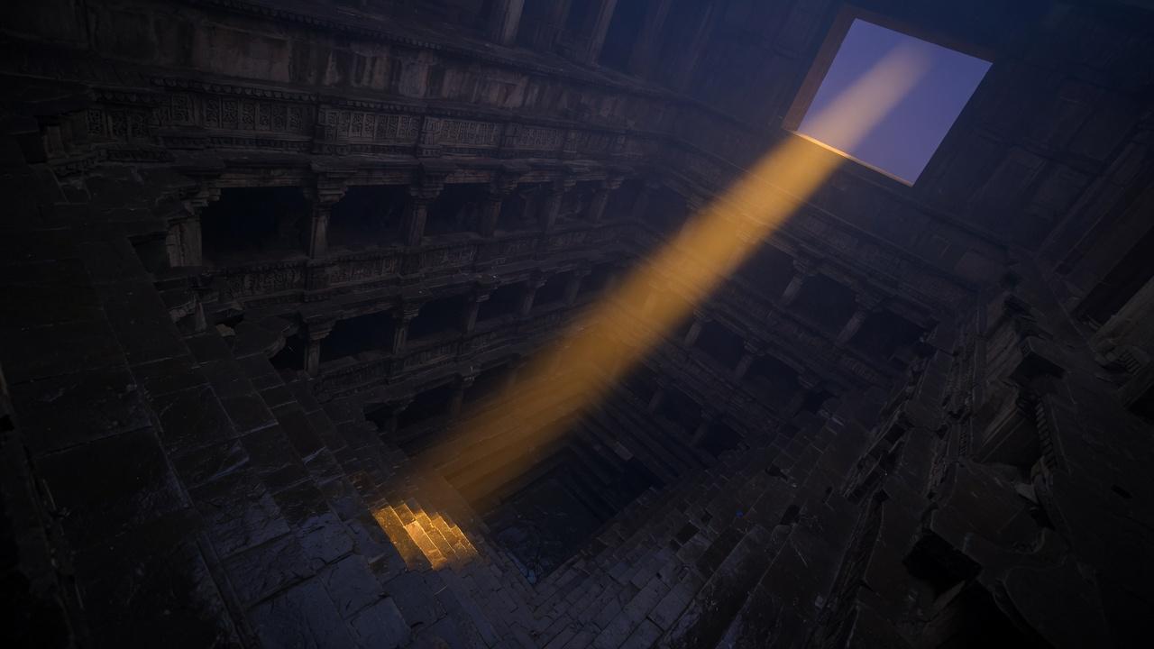 An ancient stepwell at night, a shaft of saffron light falling through dark stone